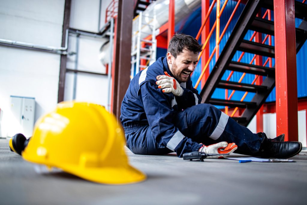 An injured employee laying on the ground holding his shoulder in pain.